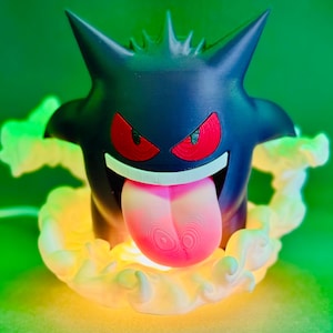 May include: A black Gengar lamp with red eyes and a pink tongue. The lamp is surrounded by a glowing, yellow-green aura. The design is based on the popular Pokemon character.