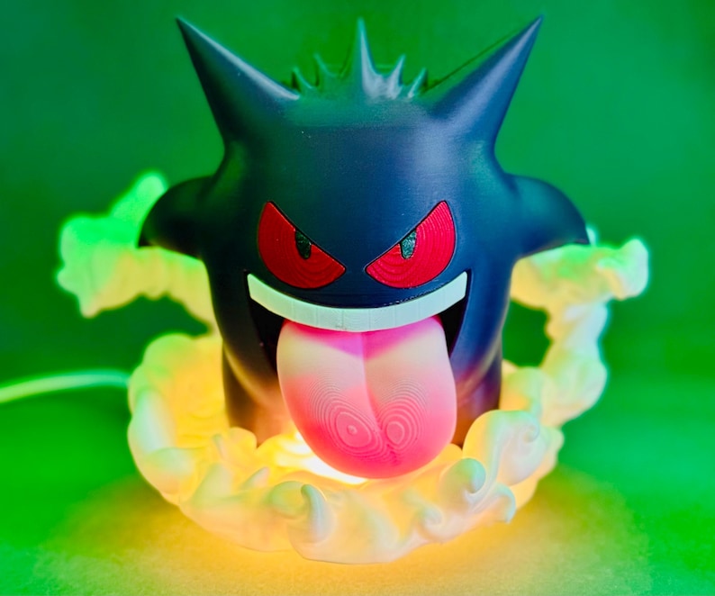May include: A black Gengar lamp with red eyes and a pink tongue. The lamp is surrounded by a glowing, yellow-green aura. The design is based on the popular Pokemon character.