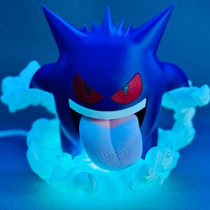 May include: A blue Gengar figure with red eyes and a long, pink tongue. The figure is surrounded by a glowing, light blue cloud effect. The design is inspired by the popular Pok&eacute;mon franchise.