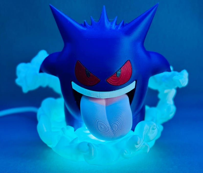 May include: A blue Gengar figure with red eyes and a long, pink tongue. The figure is surrounded by a glowing, light blue cloud effect. The design is inspired by the popular Pok&eacute;mon franchise.
