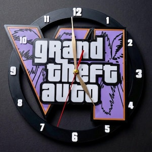 May include: A circular black wall clock featuring the Grand Theft Auto V logo in white text over a purple background with palm tree silhouettes. The clock face has white numbers from 1 to 12 around the perimeter and gold-coloured clock hands.