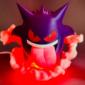 May include: A purple Gengar lamp with red eyes and a long pink tongue. The lamp is surrounded by a cloud of white smoke and emits a red glow. The design is based on the popular Pokemon character.