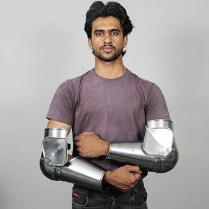 May include: Polished steel arm armour, including elbow and forearm protection. The armour is riveted together and has a reflective surface. The design is for historical reenactment or costume use. The metal has a bright, silver colour.