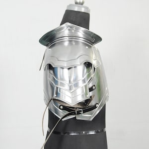 May include: A shiny silver shoulder armour piece, with layered plates and a curved design. The armour is displayed on a black form, highlighting its intricate details and reflective surface. Leather straps and buckles secure the armour.