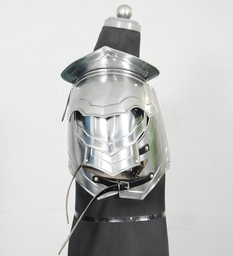 May include: A shiny silver shoulder armour piece, with layered plates and a curved design. The armour is displayed on a black form, highlighting its intricate details and reflective surface. Leather straps and buckles secure the armour.