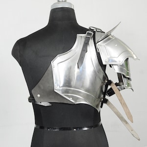 May include: A polished steel shoulder armour piece with a layered design, featuring a prominent shoulder spike. The armour is attached to a black leather backing and secured with leather straps. The piece is displayed on a black mannequin.