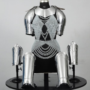 Könnte beinhalten: Eine vollständige mittelalterliche Rüstung, einschließlich Brustplatte, Schulterpanzer und Arm- und Beinschutz. Die Rüstung besteht aus poliertem Silbermetall und Kettenhemd, ausgestellt auf einer schwarzen Schaufensterpuppe.