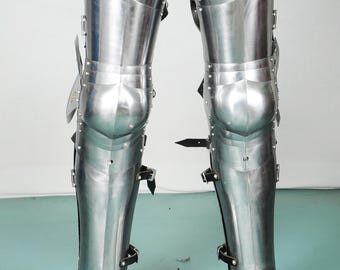 May include: Full leg armor made of polished steel. The armor includes articulated plates for the thighs, knees, shins, and feet. Black leather straps and buckles secure the pieces. The armor is designed to protect the legs.