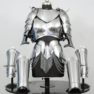 May include: A complete set of polished silver medieval armor, including a breastplate, shoulder guards, arm and leg protection. The armor is displayed on a black mannequin, with chainmail and leather straps.