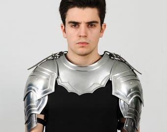 Peut inclure: Une armure d'épaule de couleur argentée, comprenant des plaques articulées et une protection de cou. L'armure est conçue pour protéger les épaules et le haut de la poitrine. L'armure métallique est portée sur une chemise noire, suggérant un thème médiéval ou fantastique.