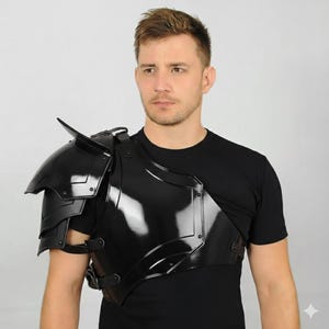 May include: Black shoulder armour with a glossy finish. The armour features layered plates and a pointed shoulder guard. It is secured with straps and buckles. The armour is designed to protect the shoulder and chest area.