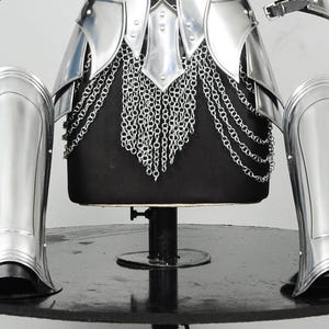 K&ouml;nnte beinhalten: Ein Set aus polierten, silberfarbenen Metallr&uuml;stungsteilen, bestehend aus einer Brustplatte mit Kettenhemdrock, zwei Armschienen und zwei Beinschienen. Die R&uuml;stung weist glatte, reflektierende Oberfl&auml;chen sowie bewegliche Teile mit Nieten auf.