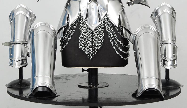 K&ouml;nnte beinhalten: Ein Set aus polierten, silberfarbenen Metallr&uuml;stungsteilen, bestehend aus einer Brustplatte mit Kettenhemdrock, zwei Armschienen und zwei Beinschienen. Die R&uuml;stung weist glatte, reflektierende Oberfl&auml;chen sowie bewegliche Teile mit Nieten auf.