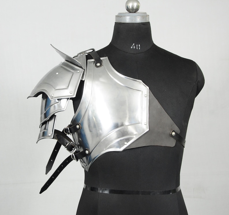 May include: A shiny silver shoulder armour piece with layered plates and a pointed edge. The armour is secured with black leather straps and buckles. The piece is displayed on a black mannequin.