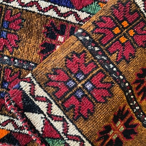 May include: A woven textile rug featuring a brown background with repeating geometric floral patterns in red, black, white, and orange. The design includes thick horizontal bands with intricate, symmetrical motifs and a textured pile surface.