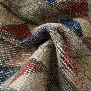 K&ouml;nnte beinhalten: Nahaufnahme eines gefalteten Teppichs mit geometrischem Muster. Der Teppich weist eine Mischung aus Farben auf, darunter Beige, Rot, Blau und Gr&uuml;n. Die Textur des Teppichs ist sichtbar, mit einem gewebten Aussehen. Der Teppich ist wahrscheinlich aus Wolle oder einem &auml;hnlichen Material.