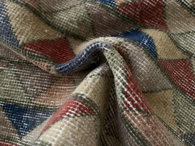 K&ouml;nnte beinhalten: Nahaufnahme eines gefalteten Teppichs mit geometrischem Muster. Der Teppich weist eine Mischung aus Farben auf, darunter Beige, Rot, Blau und Gr&uuml;n. Die Textur des Teppichs ist sichtbar, mit einem gewebten Aussehen. Der Teppich ist wahrscheinlich aus Wolle oder einem &auml;hnlichen Material.