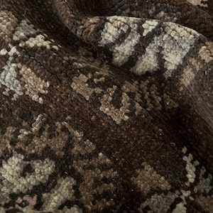 May include: Close-up of a textured rug with a repeating pattern. The rug features a mix of brown, beige, and gray tones, creating a neutral and earthy aesthetic. The fabric appears soft and plush, suggesting comfort and warmth.