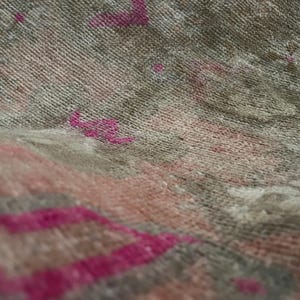 May include: Close-up of a woven textile with a textured surface. The fabric features a blend of muted colors, including gray, pink, and beige, with accents of bright fuchsia. The design appears to be a rug or textile.