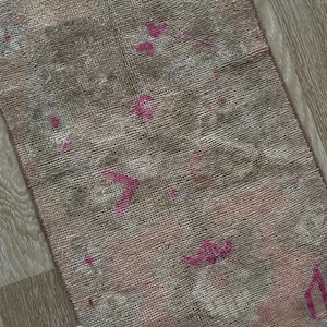 May include: A rectangular, vintage-style rug with a faded, distressed appearance. The rug features a blend of muted colors, including pink, brown, and gray, with accents of brighter pink floral patterns. The rug's texture appears soft and worn.