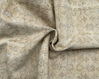 Può includere: Un tappeto in tessuto intrecciato con una base color beige chiaro e un motivo ripetuto di sottili contorni floreali marrone scuro e blu tenue. Il tessuto presenta una trama strutturata a griglia con pieghe morbide che creano profondità.