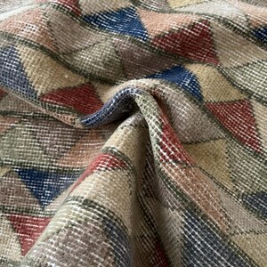 K&ouml;nnte beinhalten: Nahaufnahme eines gewebten Teppichs mit geometrischem Muster. Der Teppich weist ein sich wiederholendes Design aus Dreiecken in Beige-, Rot-, Blau- und Gr&uuml;nt&ouml;nen auf. Die Textur des Teppichs ist sichtbar, mit einem leicht abgenutzten Aussehen.
