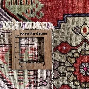 May include: Close-up of a section of a vintage rug with a wooden ruler that reads "Knots Per Square" in the image. The rug features a complex geometric pattern in red, green, purple, and beige. The ruler shows measurements in inches and centimeters.