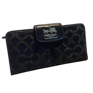 May include: Black Coach wallet with a repeating pattern of interlocking "C" shapes. The wallet has a flap closure with a silver emblem of a horse-drawn carriage. The wallet is rectangular and made of a textured material.