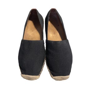 以下が含まれることがあります： 黒いエスパドリーユのスリッポンシューズのペア。靴はキャンバスのアッパー、天然色の織りジュートソール、茶色の革製インソールを備えています。カジュアルウェア向けに設計されています。
