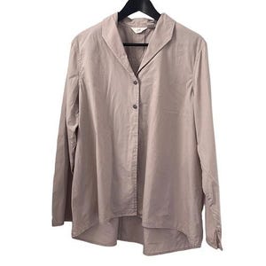 May include: A light brown button-down shirt with long sleeves, hanging on a black hanger. The shirt has a wide collar and a slightly asymmetrical hemline. The fabric appears to be a lightweight cotton or linen blend.