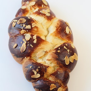 May include: A braided loaf of bread, golden brown with darker, caramelized sections. Sliced almonds are scattered across the top. The bread is a rich, inviting color, suggesting a delicious, freshly baked treat.
