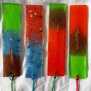 Puede incluir: Cuatro marcapáginas rectangulares de resina con superficies lisas y esquinas redondeadas. Cada marcapáginas presenta un degradado de color único, incluyendo combinaciones de verde, azul, marrón, naranja y rojo, con purpurina incrustada.