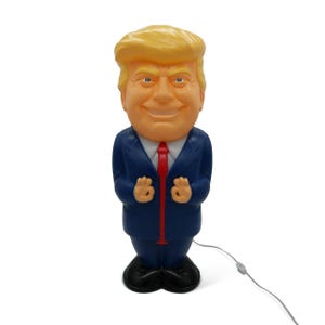 May include: A novelty lamp shaped like a smiling man with blonde hair, blue eyes, and a blue suit with a red tie. The lamp has a black base and a power cord.
