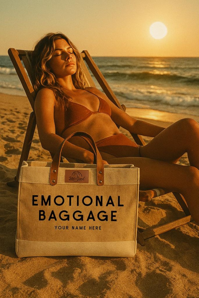 May include: A beige tote bag with the words "EMOTIONAL BAGGAGE" printed in black. The bag has brown leather handles and a small label that says "This Good". The bag is on a sandy beach.