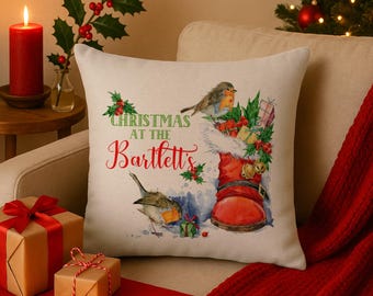 Könnte beinhalten: Ein dekoratives Weihnachtskissen mit festlichem Design. Das Kissen zeigt einen roten Weihnachtsmannstiefel, gefüllt mit Geschenken und Grünzeug, mit zwei Vögeln in der Nähe. Der Text "Christmas at the Bartlett's" ist auf dem Kissen aufgedruckt.