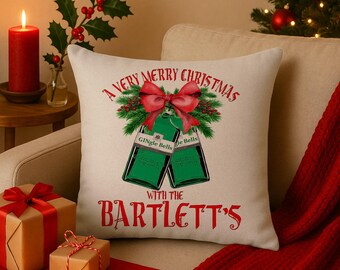 Könnte beinhalten: Ein cremefarbenes Weihnachtskissen mit dem Text "A Very Merry Christmas with the Bartlett's". Das Kissen zeigt ein Design von zwei grünen Flaschen mit roten Schleifen und den Worten "Gingle Bells".