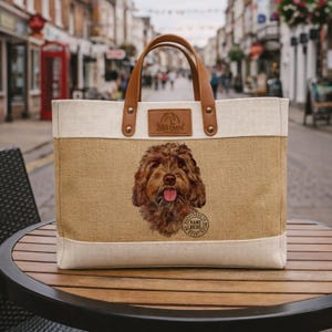 Könnte beinhalten: Beige Tragetasche mit einer braunen Hundeillustration. Die Tasche hat braune Ledergriffe und einen kleinen Lederaufnäher mit dem Text "Life's Good". Eine kreisförmige Grafik mit dem Text "Happiness is Name Here Loved" ist ebenfalls sichtbar.