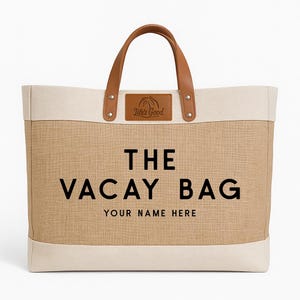 May include: A large beige and cream tote bag with brown leather handles and accents. The bag features the text "THE VACAY BAG" in black, with space for personalization below. A leather patch reads "Life's Good".