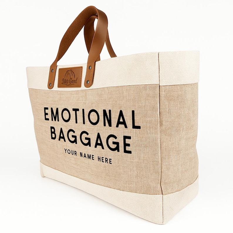 May include: A beige tote bag with the words "EMOTIONAL BAGGAGE" printed in black. The bag has brown leather handles and a cream-colored top and bottom trim. The text "YOUR NAME HERE" is printed below the main text.