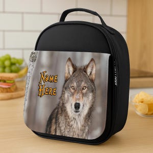 May include: Black insulated lunch bag with a handle. The front features a close-up of a wolf with the text "NAME HERE" in orange. The bag is designed to keep food and drinks cold.