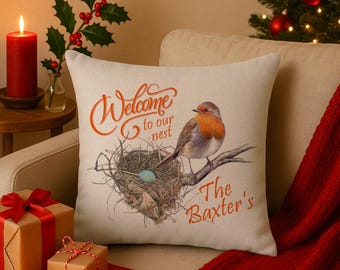 Könnte beinhalten: Beiges quadratisches Zierkissen mit einem Aufdruck. Das Design zeigt einen Vogel auf einem Ast über einem Nest mit einem blauen Ei. Der orangefarbene Text lautet "Welcome to our nest" und "The Baxter's".