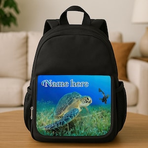 May include: Black backpack featuring a vibrant underwater scene with a sea turtle and the text "Name here". The backpack has side pockets and a top handle. The image shows a sea turtle.
