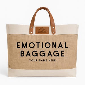 May include: A beige tote bag with the words "EMOTIONAL BAGGAGE" in large black letters. The bag has brown leather handles and a small leather patch with the text "Life's Good". The bottom of the bag has the text "YOUR NAME HERE".