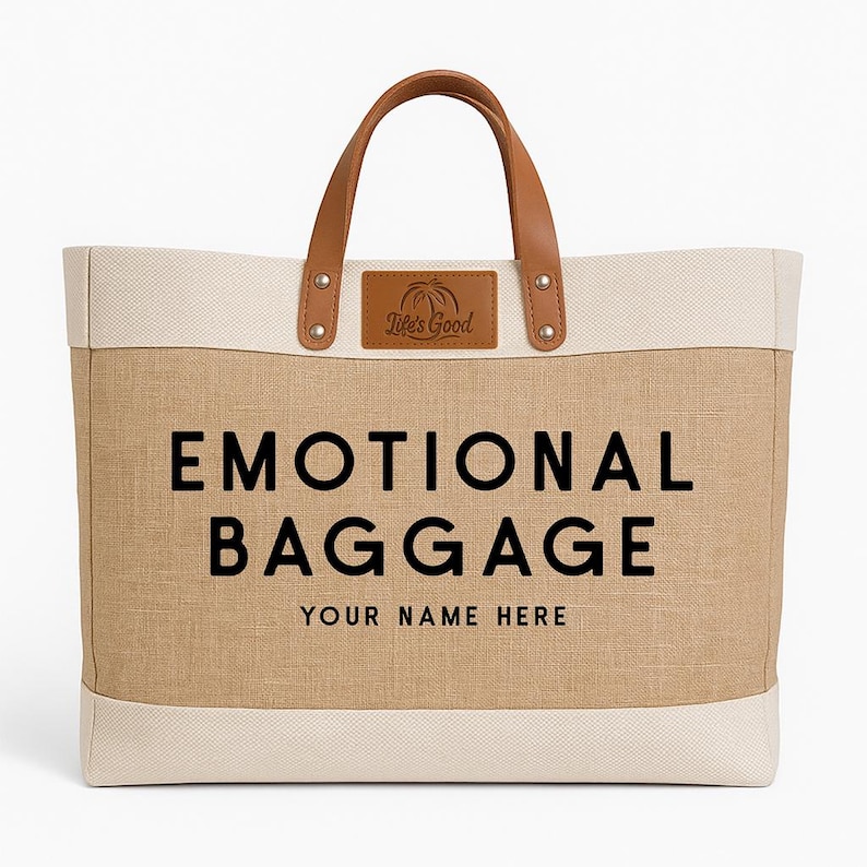 May include: A beige tote bag with the words "EMOTIONAL BAGGAGE" in large black letters. The bag has brown leather handles and a small leather patch with the text "Life's Good". The bottom of the bag has the text "YOUR NAME HERE".