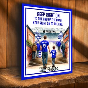 Peut inclure: Impression encadrée avec bordure bleue, représentant un père et son enfant montant des marches vers un stade. Le texte dit "KEEP RIGHT ON" et "ST ANDREWS". Le père et l'enfant portent des maillots bleus avec les numéros 9 et 7.