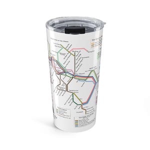 Pode incluir: Caneca de viagem branca com um design de mapa com linhas coloridas e texto, assemelhando-se a uma rede de transportes urbanos. A caneca tem uma tampa preta. O design do mapa é uma representação estilizada de um sistema de transportes urbanos.