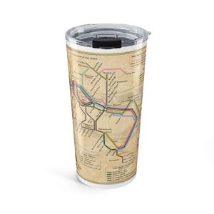 Pode incluir: Uma caneca de viagem branca com um design de mapa. O mapa apresenta várias linhas e texto, com um sistema de código de cores. A caneca tem uma tampa preta com fecho deslizante. O esquema de cores geral é bege, castanho e várias cores para as linhas do mapa.