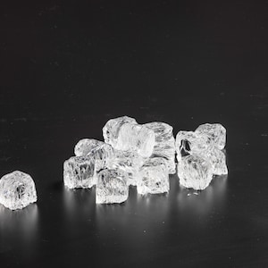 May include: A collection of small, clear, irregular acrylic ice cubes with a faceted, textured surface that mimics the appearance of frozen water. These decorative pieces are transparent and have a glossy finish, arranged in a cluster.