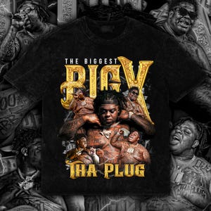 May include: Black t-shirt with a gold graphic design. The design features the text "THE BIGGEST BIGX THA PLUG" and multiple images of a person with tattoos. The t-shirt has a distressed, vintage appearance.