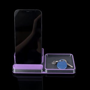 May include: A purple and gray phone and key organizer. The organizer has a slot for a smartphone and a small tray holding keys. The design is modern and minimalist, with a sleek, clean aesthetic.